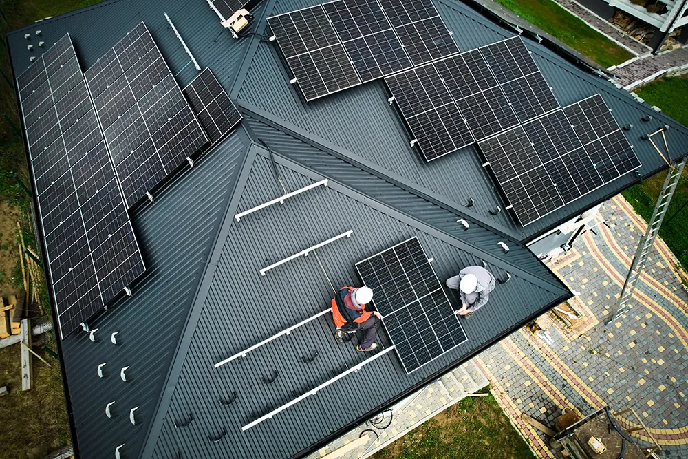 Ingenieure bauen Photovoltaik-Solarmodulstation auf dem Dach eines Hauses. Männer Elektriker in Helmen bei der Installation von Solarmodulsystemen im Freien. Konzept der alternativen und erneuerbaren Energie.